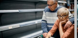 Worried elderly couple before empty supermarket shelves.