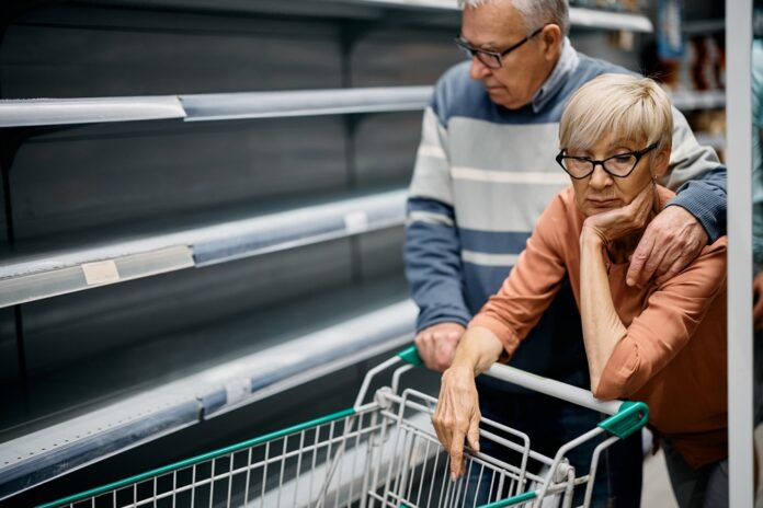 Worried elderly couple before empty supermarket shelves.