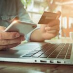 Person using credit card and smartphone near laptop.