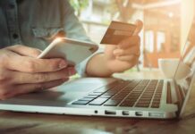 Person using credit card and smartphone near laptop.