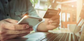 Person using credit card and smartphone near laptop.