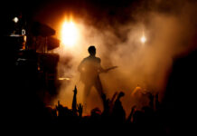 Guitarist performing on stage with audience and dramatic lighting.