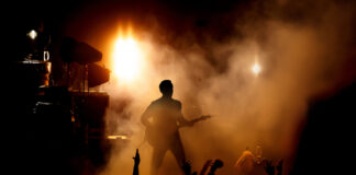 Guitarist performing on stage with audience and dramatic lighting.