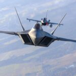 Two fighter jets flying in formation over landscape.