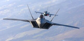 Two fighter jets flying in formation over landscape.