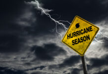 Hurricane season warning sign with lightning in stormy sky.