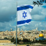 Israeli flag flying over Jerusalem skyline with Dome of Rock.