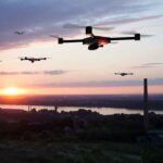 Drones flying over a landscape at sunset.