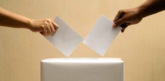 Two hands placing ballots into a voting box.