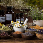 Various dried herbs in bowls and jars with fresh flowers.