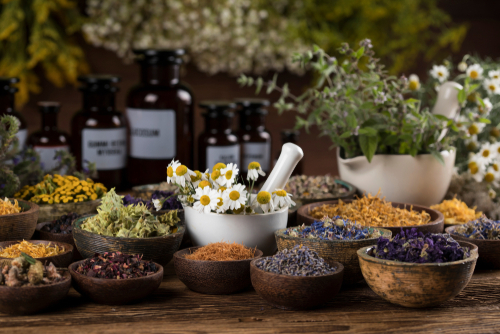 Various dried herbs in bowls and jars with fresh flowers.