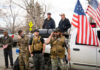 Men in military gear with American flags near truck.