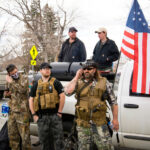 Men in military gear with American flags near truck.