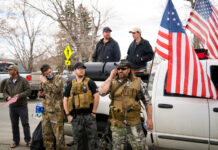 Men in military gear with American flags near truck.