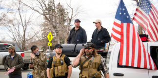 Men in military gear with American flags near truck.