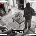 Home security footage of masked intruder with crowbar.