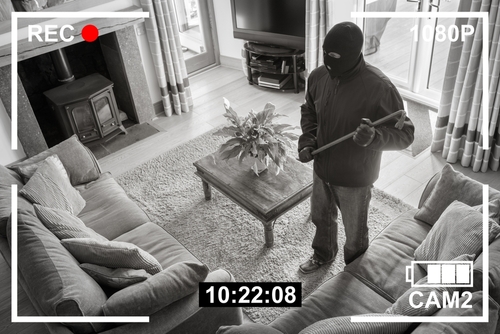 Home security footage of masked intruder with crowbar.