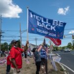 Pro-Trump supporters on street corner with 2024 flags.