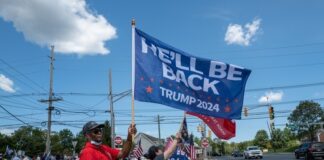 Pro-Trump supporters on street corner with 2024 flags.