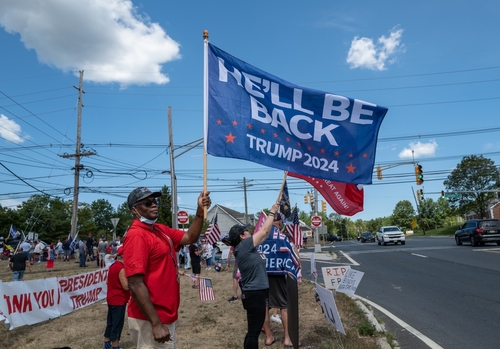 Pro-Trump supporters on street corner with 2024 flags.