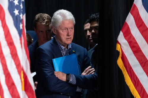 Bill Clinton standing between American flags with a folder.