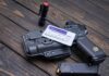 Pistol, holster, permit, flashlight, and magazine on wooden background.