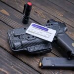 Pistol, holster, permit, flashlight, and magazine on wooden background.