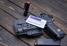 Pistol, holster, permit, flashlight, and magazine on wooden background.