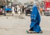 Woman in blue burqa walking through busy street scene.