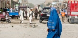 Woman in blue burqa walking through busy street scene.