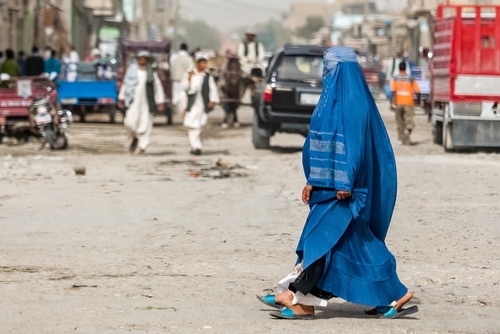 Woman in blue burqa walking through busy street scene.