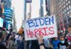 Person holding Biden Harris sign in crowded city street.