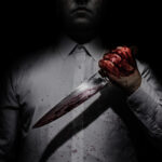 Person holding bloody knife in dark lighting.