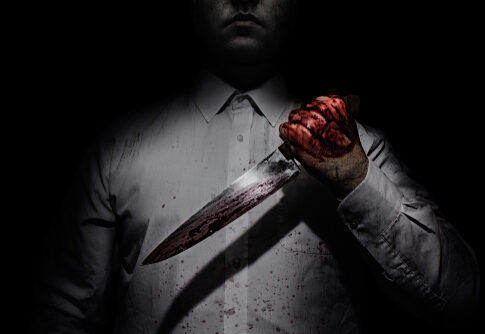 Person holding bloody knife in dark lighting.