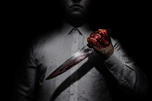 Person holding bloody knife in dark lighting.