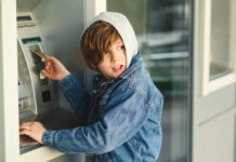 Child using an ATM machine outdoors, wearing denim jacket.