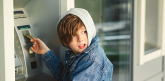 Child using an ATM machine outdoors, wearing denim jacket.