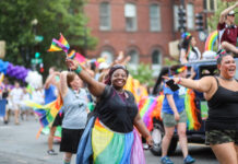 People celebrating at a pride parade, waving rainbow flags.