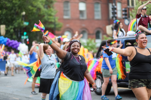 People celebrating at a pride parade, waving rainbow flags.