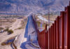 Border wall stretching through desert landscape with mountains.