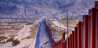 Border wall stretching through desert landscape with mountains.