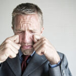 Man in suit rubbing his eyes.