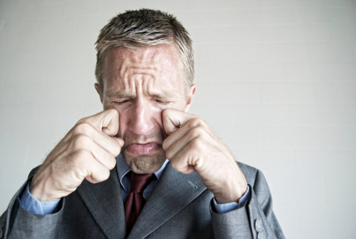 Man in suit rubbing his eyes.