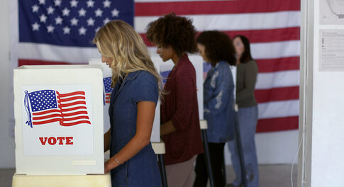 People voting in booths with U.S. flags in background.