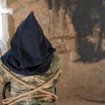 Person hooded and bound in abandoned stone room.