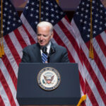 Joe Biden speaking at podium with American flags behind.