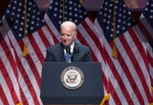 Joe Biden speaking at podium with American flags behind.