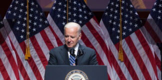 Joe Biden speaking at podium with American flags behind.