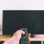 Hand holding remote towards blank TV screen.