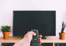 Hand holding remote towards blank TV screen.